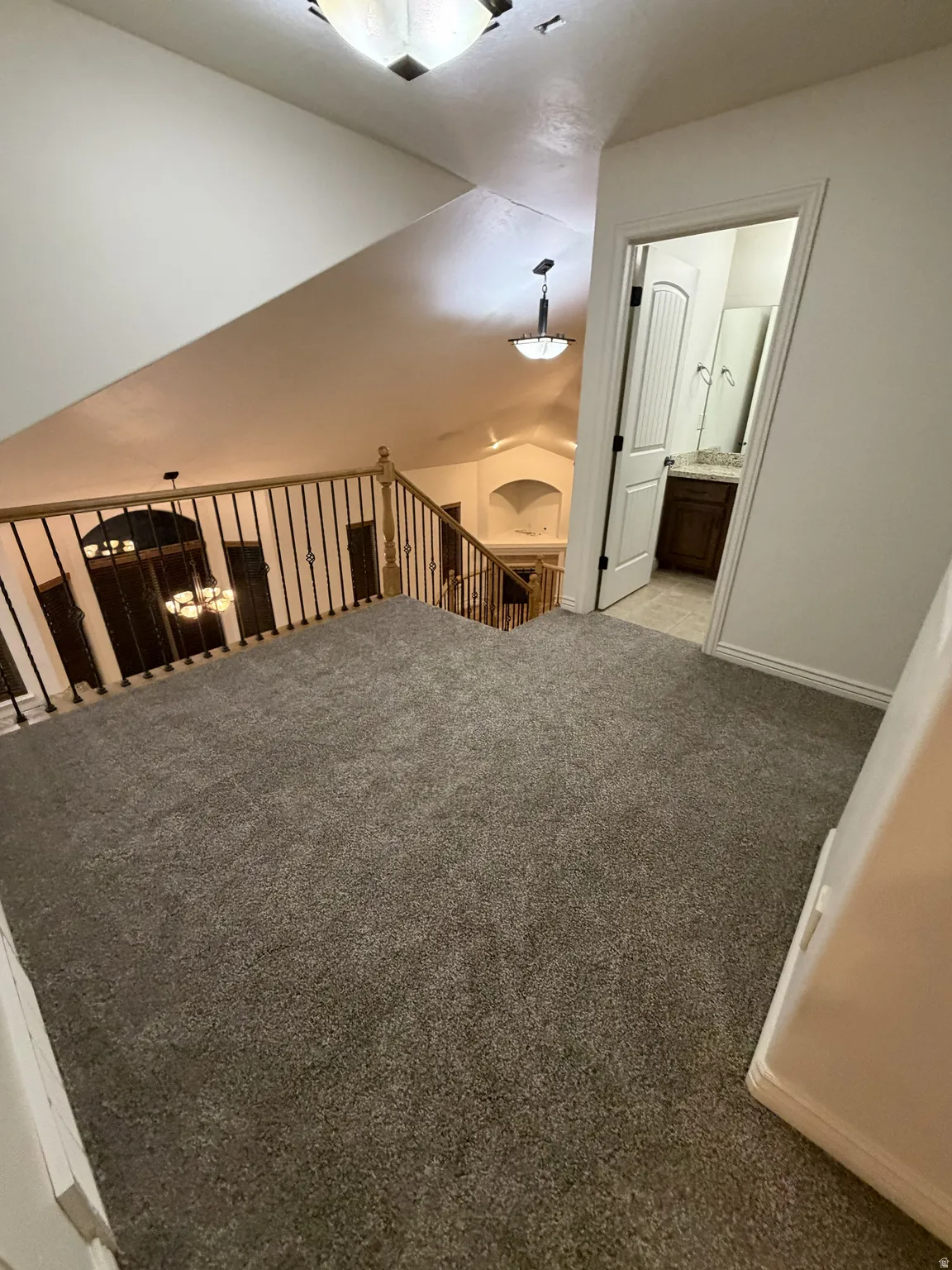 Carpeted upper landing featuring a bathroom entry, wood-finish banister, and vaulted ceilings