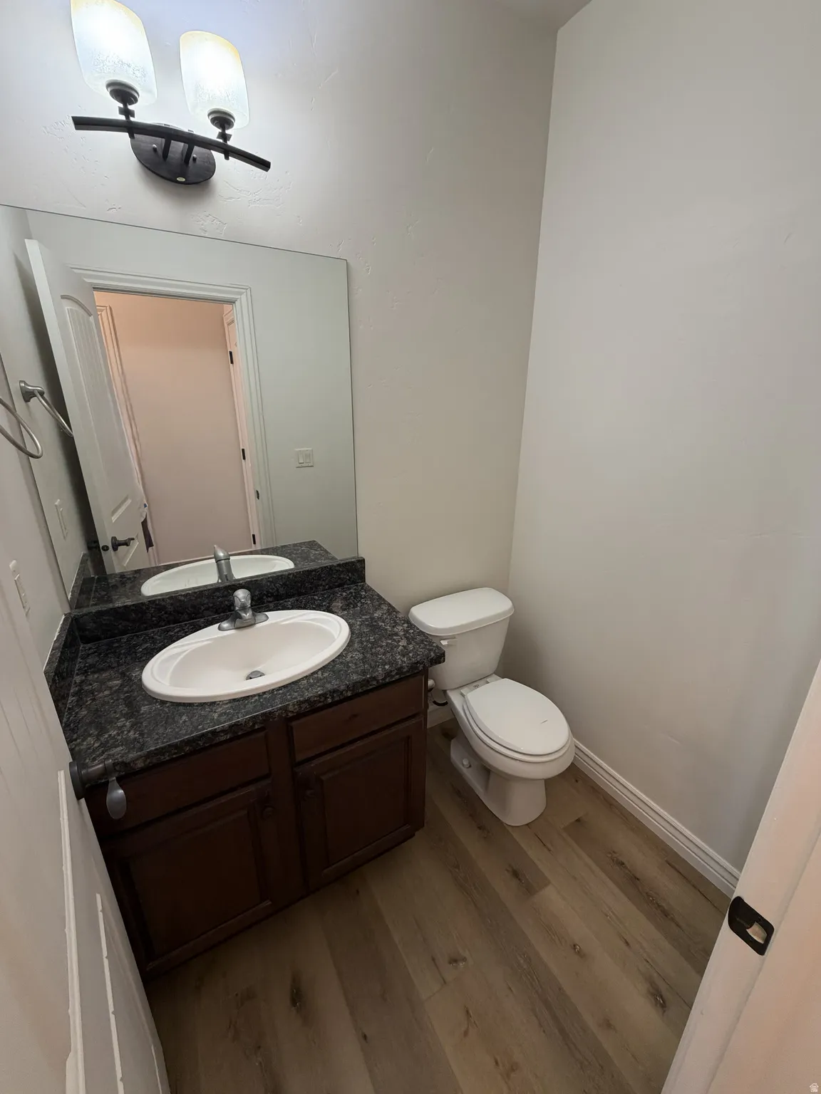 Bathroom featuring a dark wood-finish vanity with an integrated sink, a speckled countertop, and a wall-mounted mirror