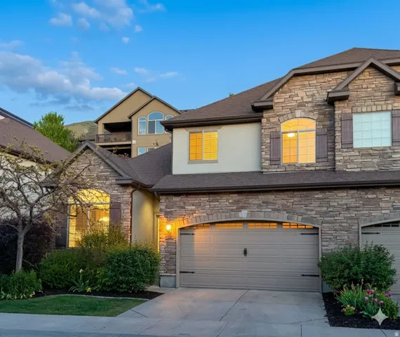 Stone and stucco exterior featuring a two-car garage with an arched opening, dark brown roof, and arched windows