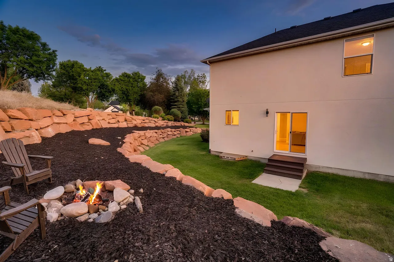 Backyard featuring a stone fire pit, tiered landscaping with natural rock walls, and a manicured lawn