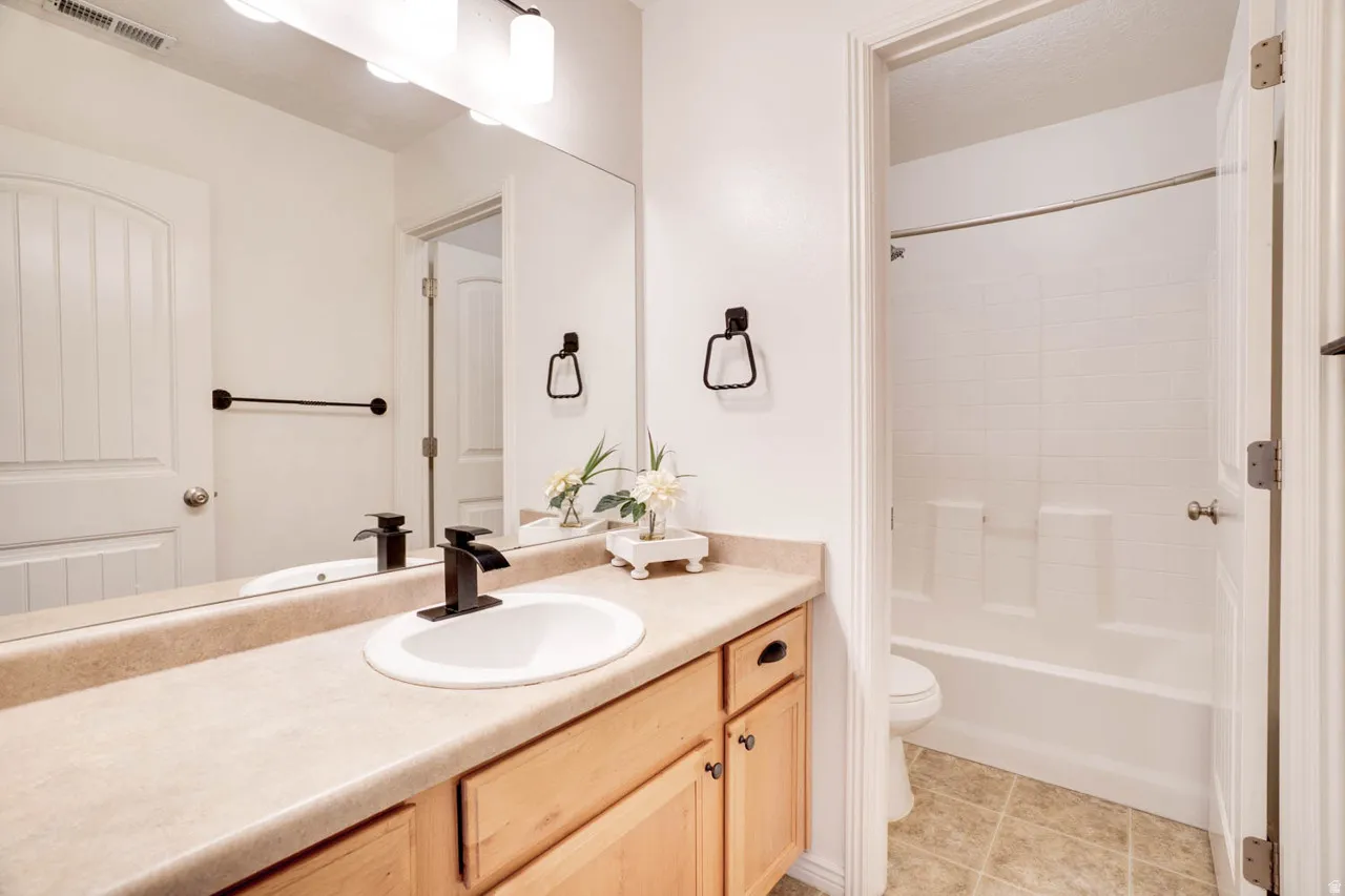 Bathroom featuring a light-toned vanity with wood-finish cabinetry, a drop-in sink with a matte black faucet, and a large wall-mounted mirror