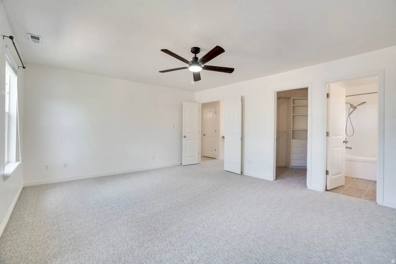 Spacious room featuring light-toned carpeting, a ceiling fan with integrated lighting, and multiple white doors