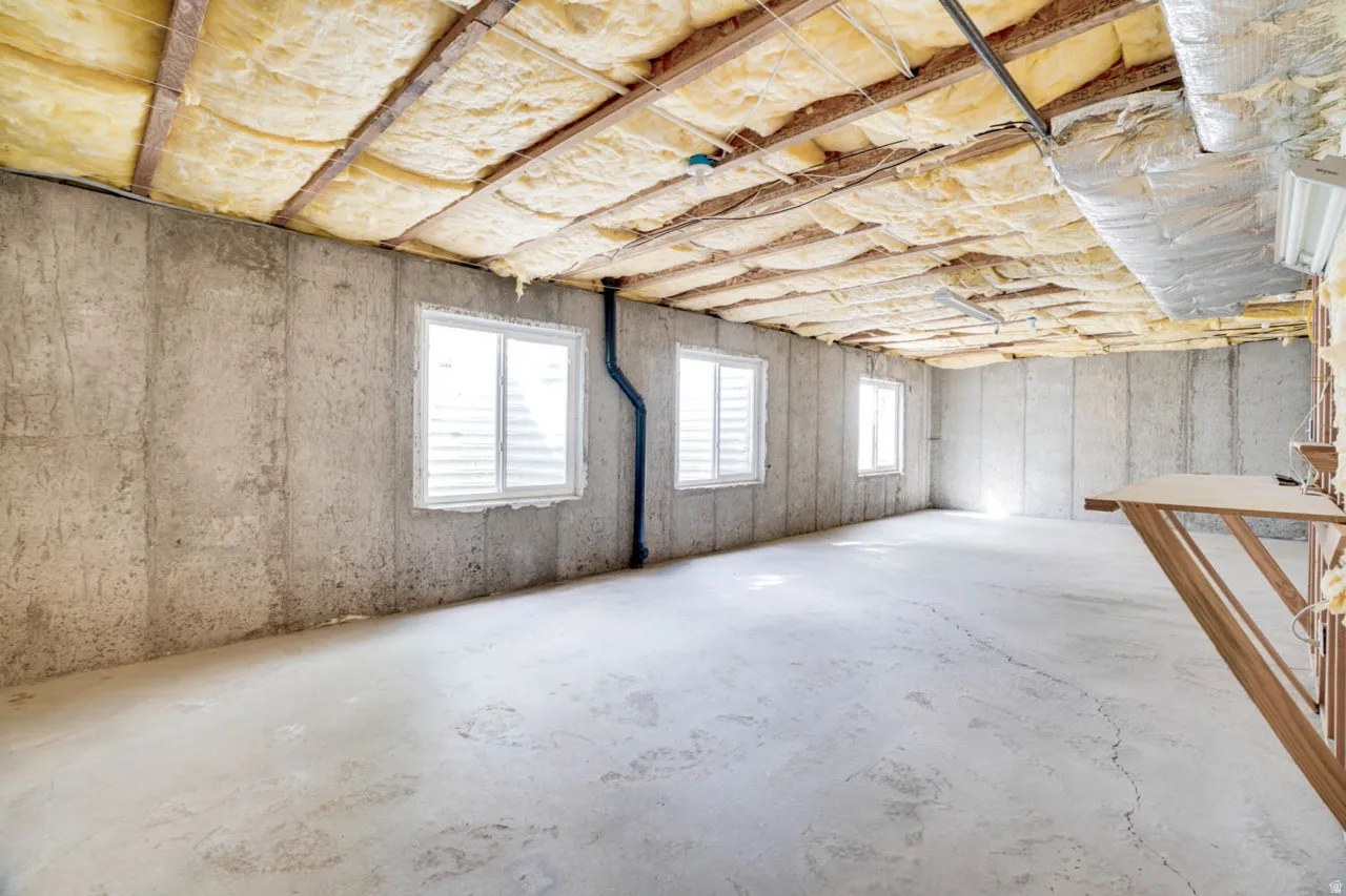 Unfinished basement featuring concrete walls, exposed insulation, three windows with white blinds, and a concrete floor