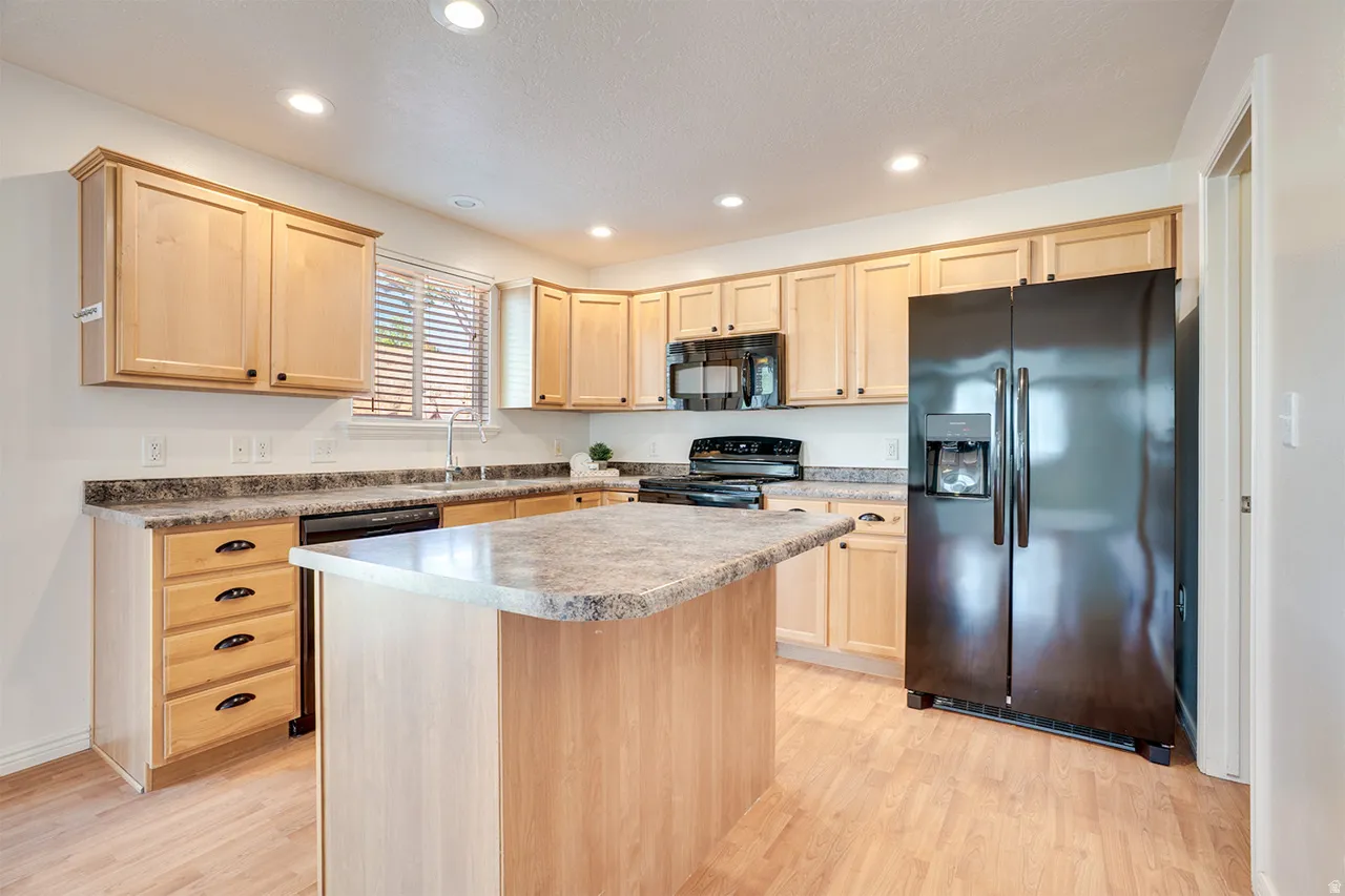 Kitchen featuring light wood cabinetry, a central island with a stone-look countertop, a black side-by-side refrigerator, recessed lighting, and wood-finish flooring