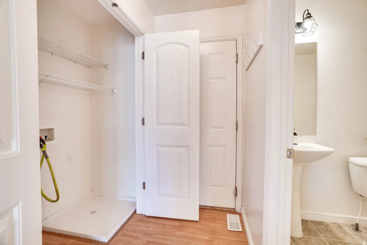 Laundry area featuring white wire shelving, a utility sink base, and wood-finish flooring