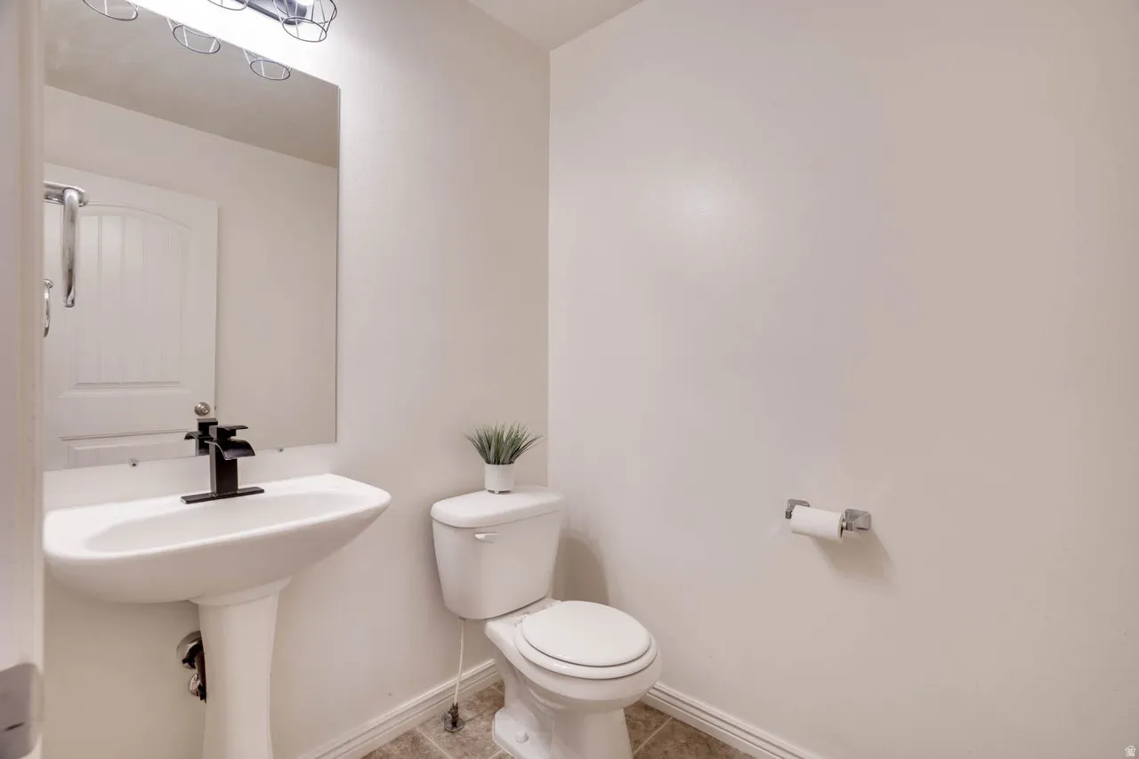 Pedestal sink with a matte black faucet, mirrored vanity, and overhead vanity lighting