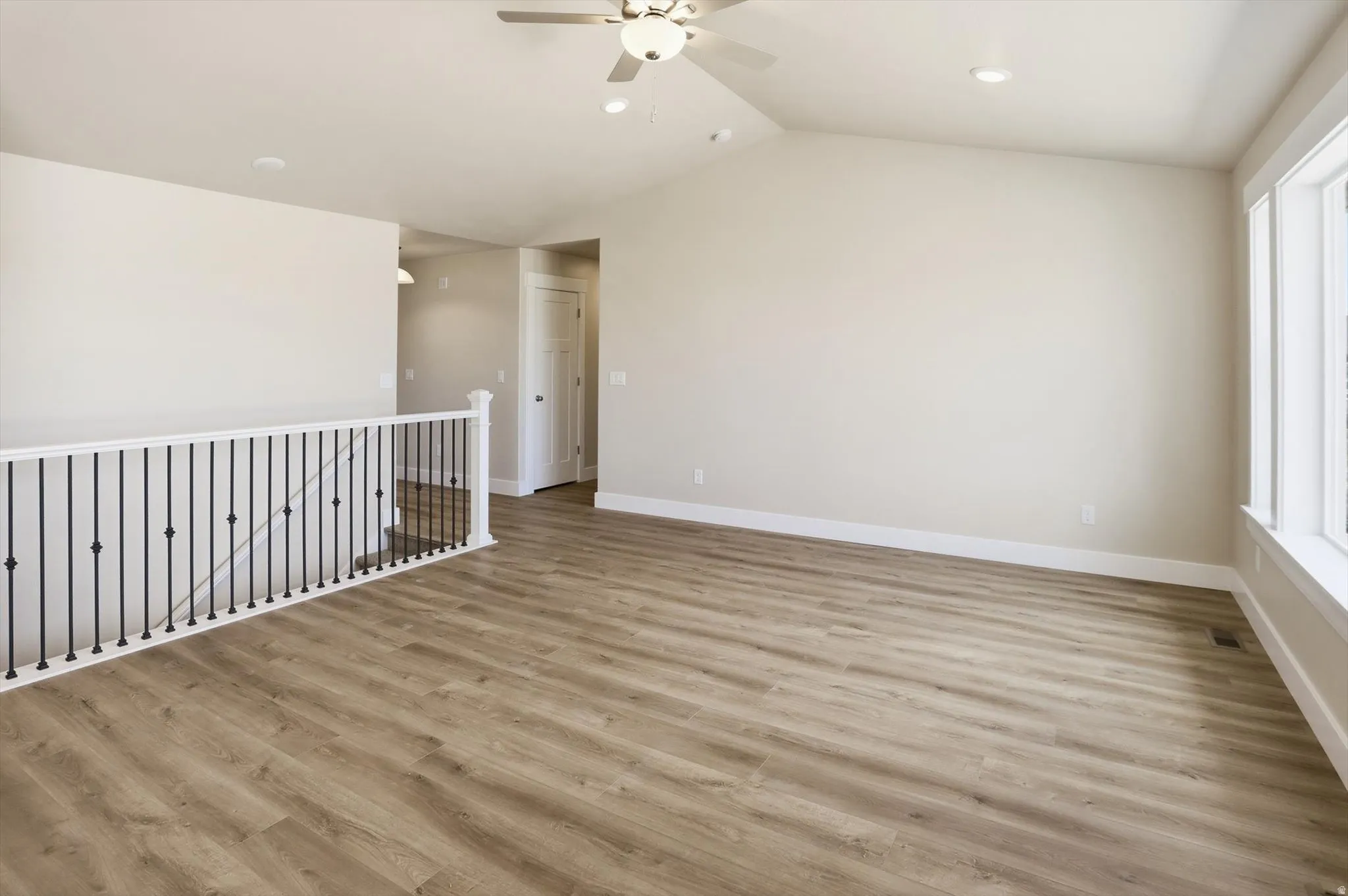 Spacious room featuring vaulted ceilings, wood-finish flooring, a contemporary ceiling fan, recessed lighting, and large windows