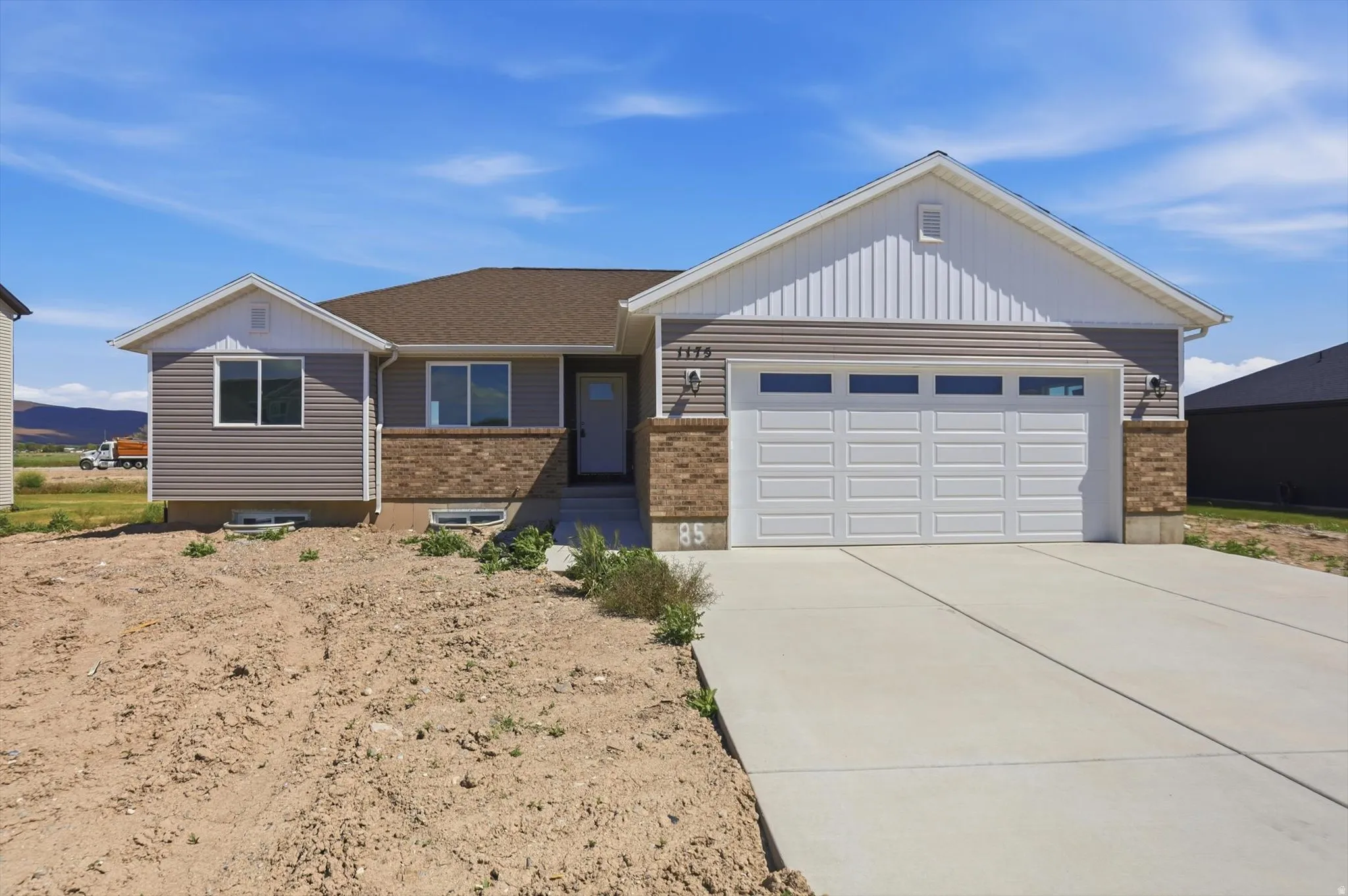 Exterior featuring light gray siding, brick accents, a two-car garage, a brown shingle roof, and a concrete driveway