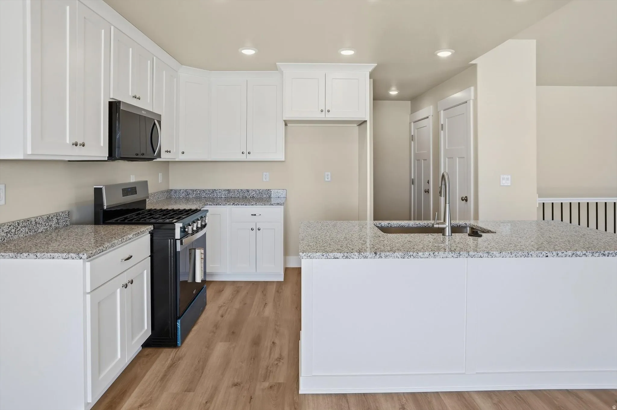 Open-concept kitchen featuring white shaker cabinetry, granite-style countertops, stainless steel appliances, and wood-finish flooring