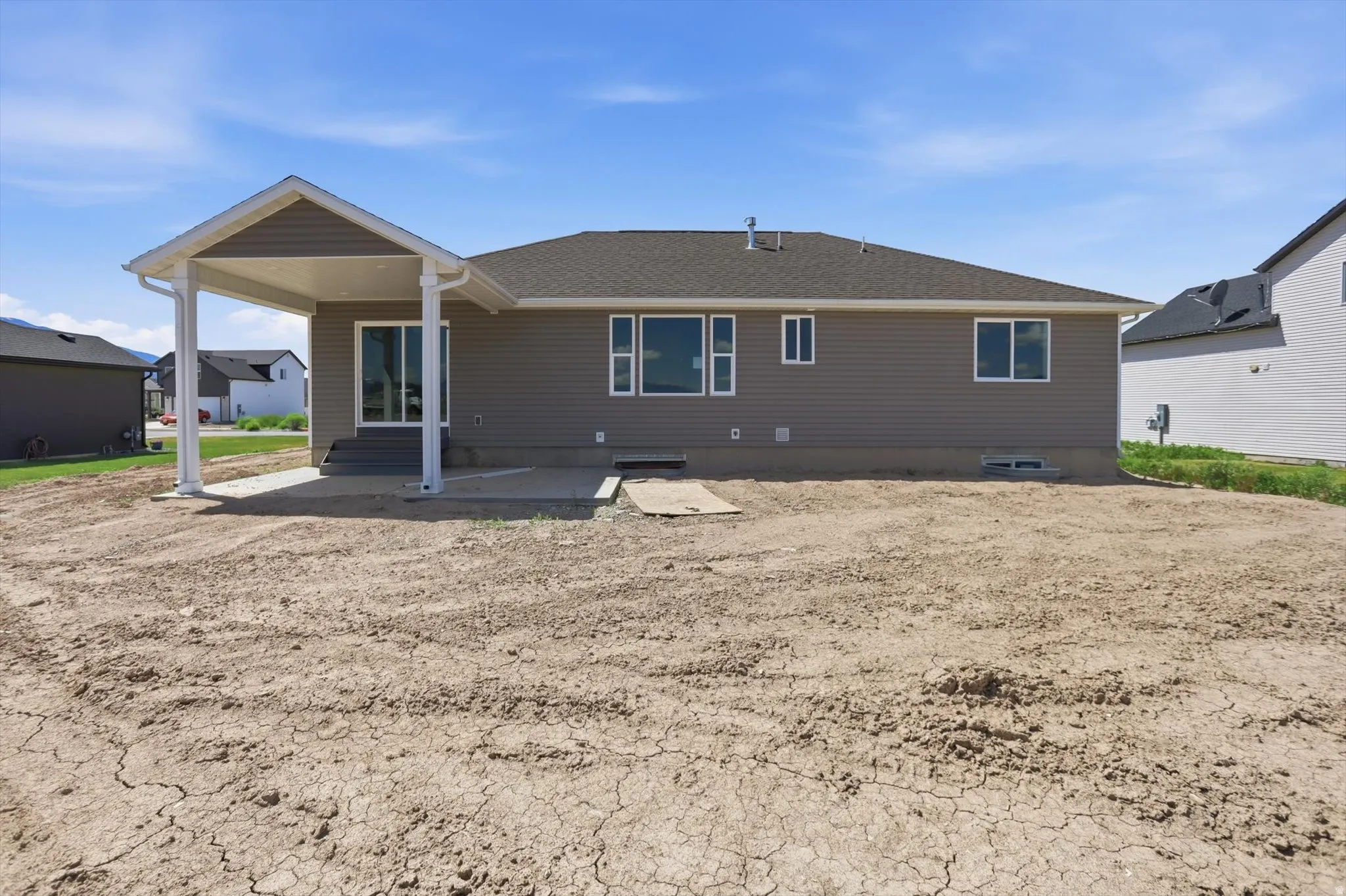 Rear exterior with covered patio, concrete pad, sliding glass door, and multiple windows
