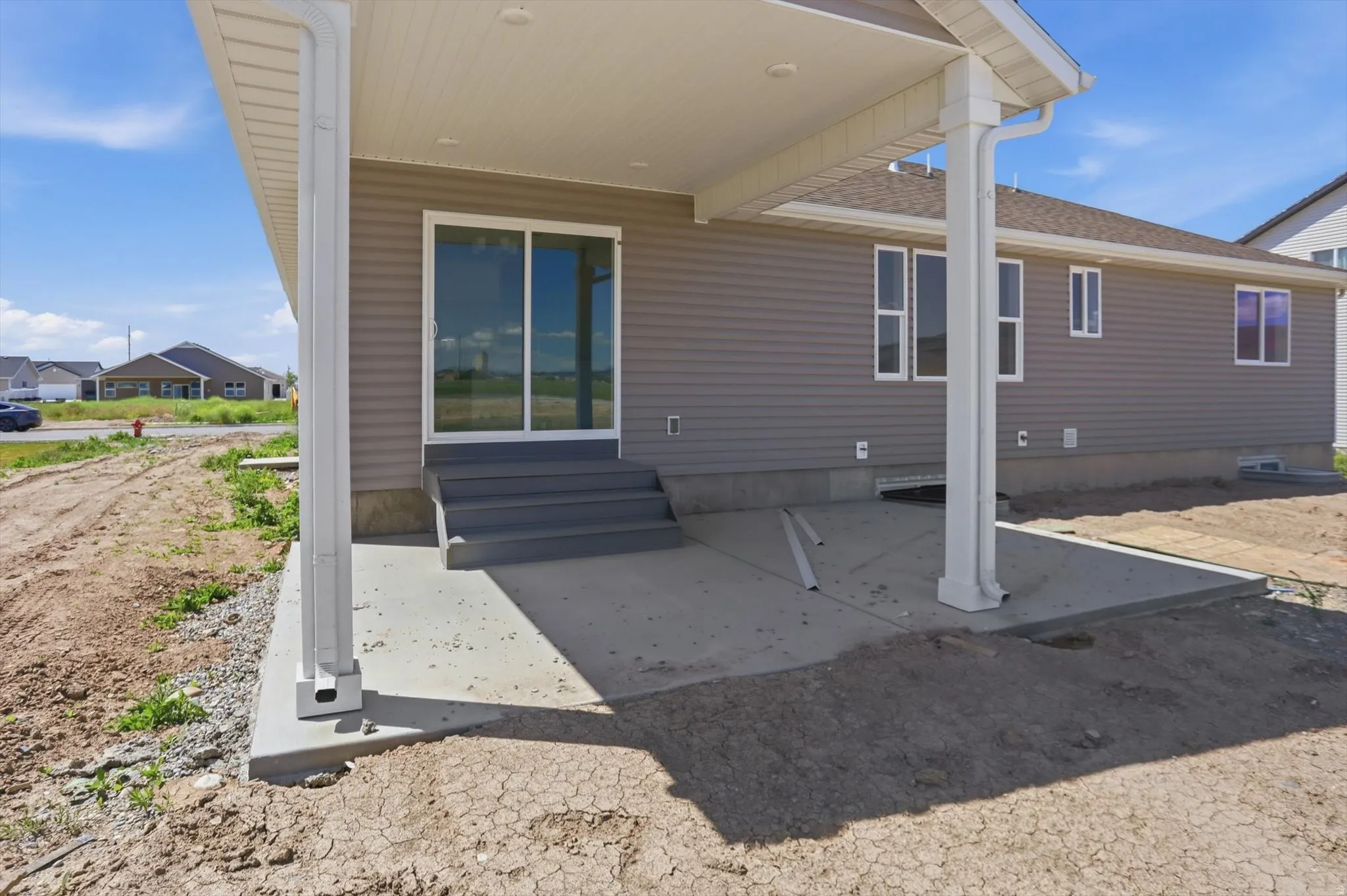 Covered concrete patio with white support columns and a gray vinyl siding exterior