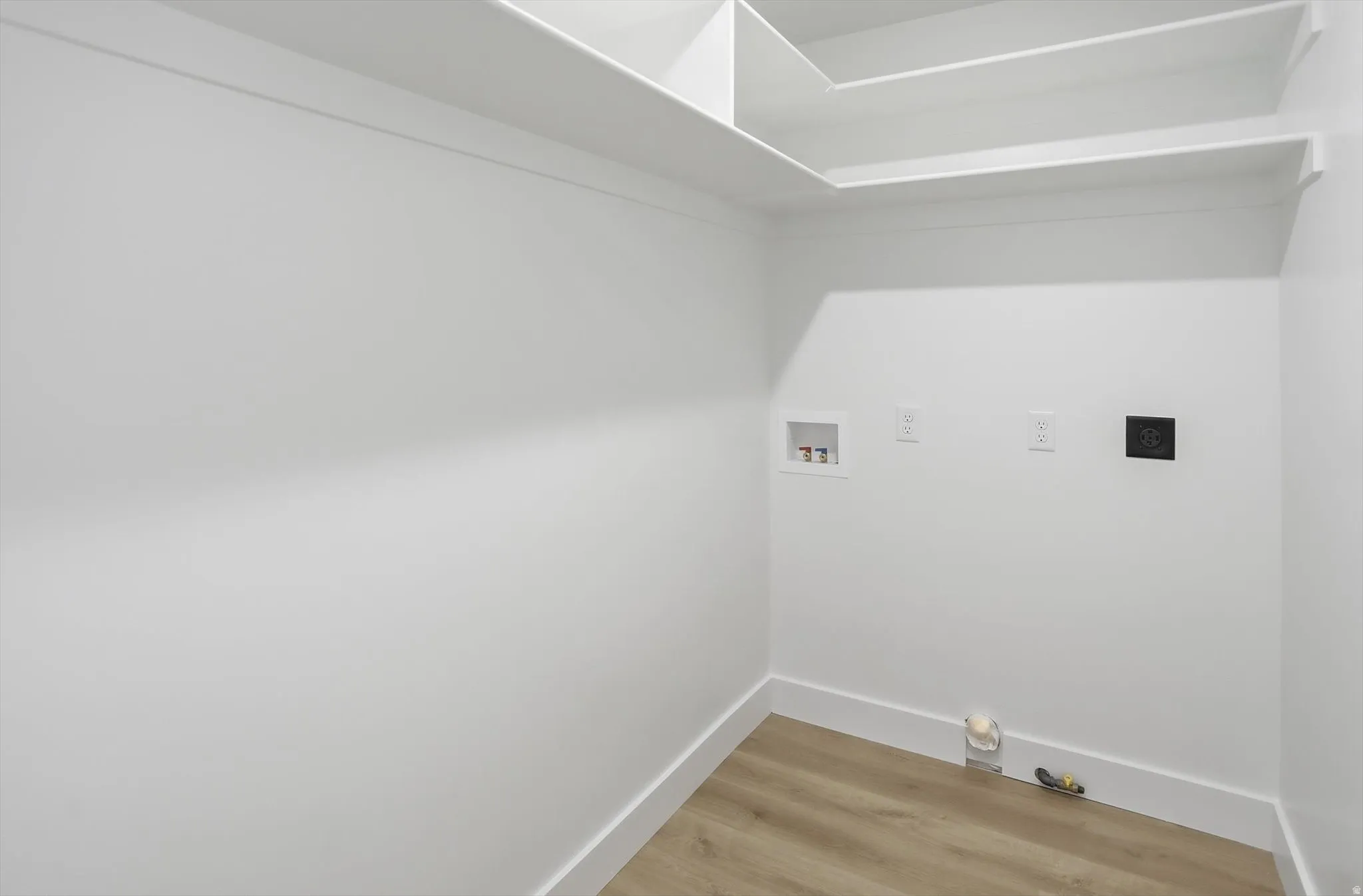 Utility room featuring wood-finish flooring, white walls, built-in shelving, and hookups