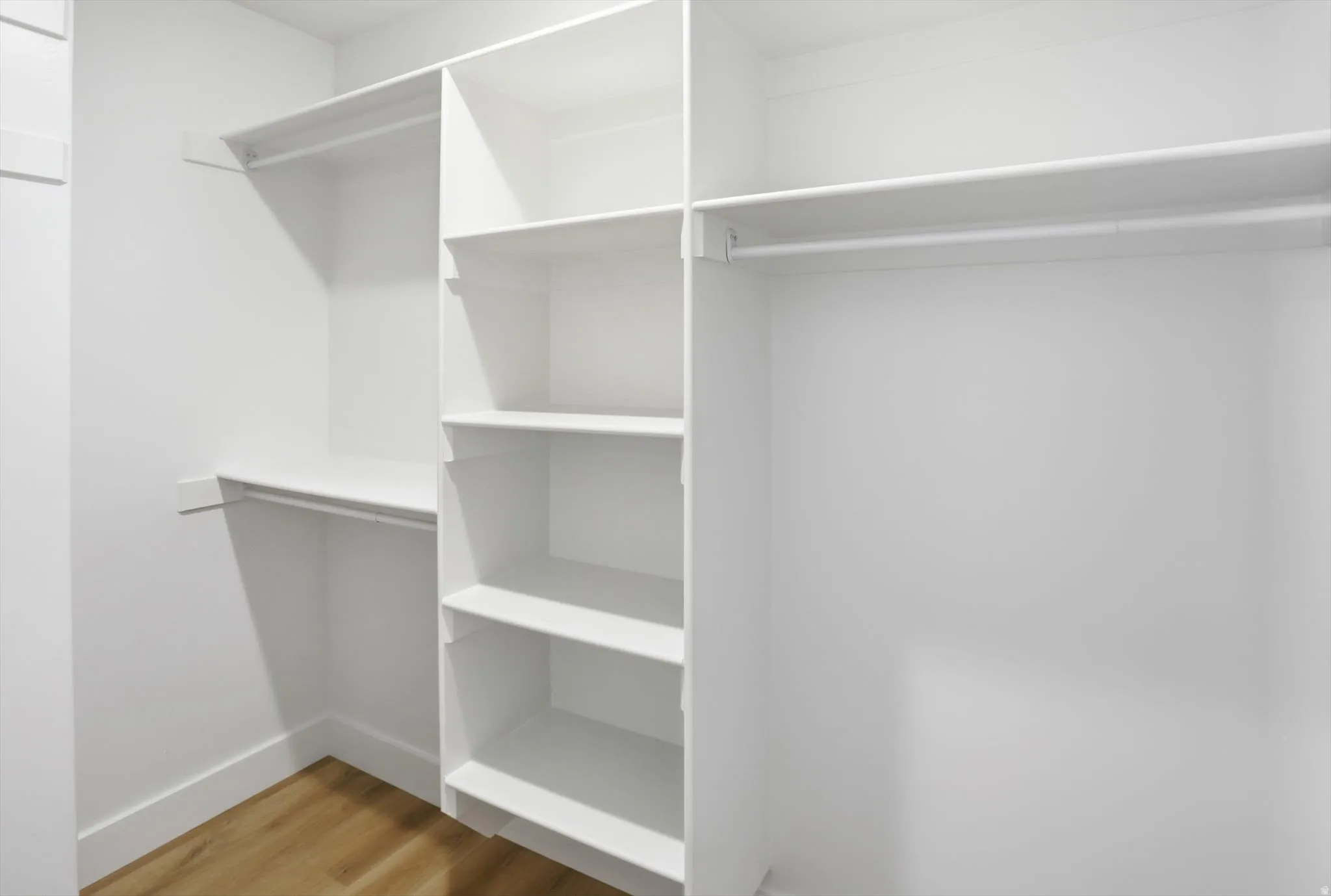 Walk-in closet featuring built-in shelving, multiple hanging rods, and wood-finish flooring