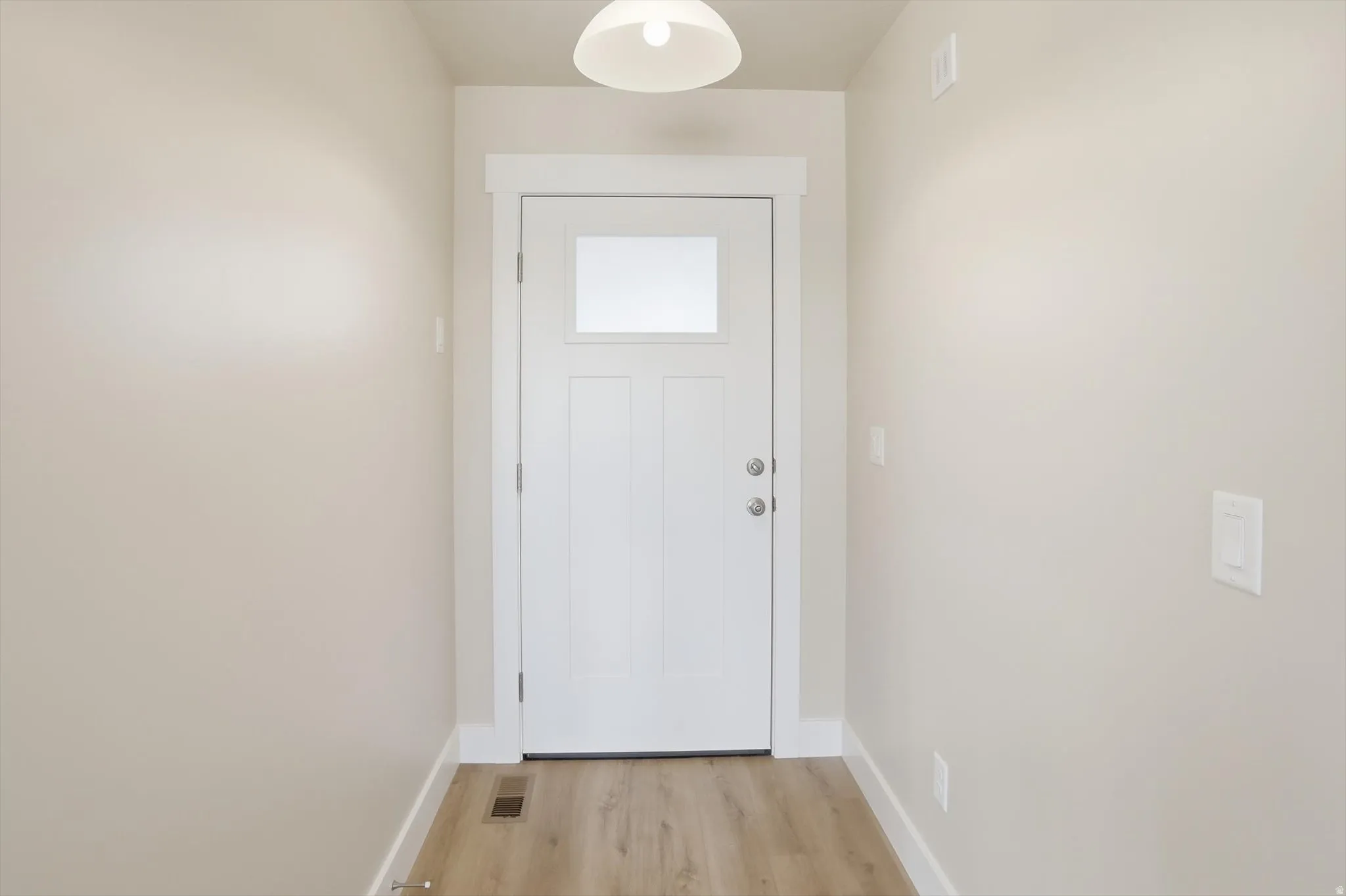 Entryway featuring a white paneled door with a rectangular window, light wood-finish flooring, light neutral-toned walls, and a ceiling-mounted light fixture