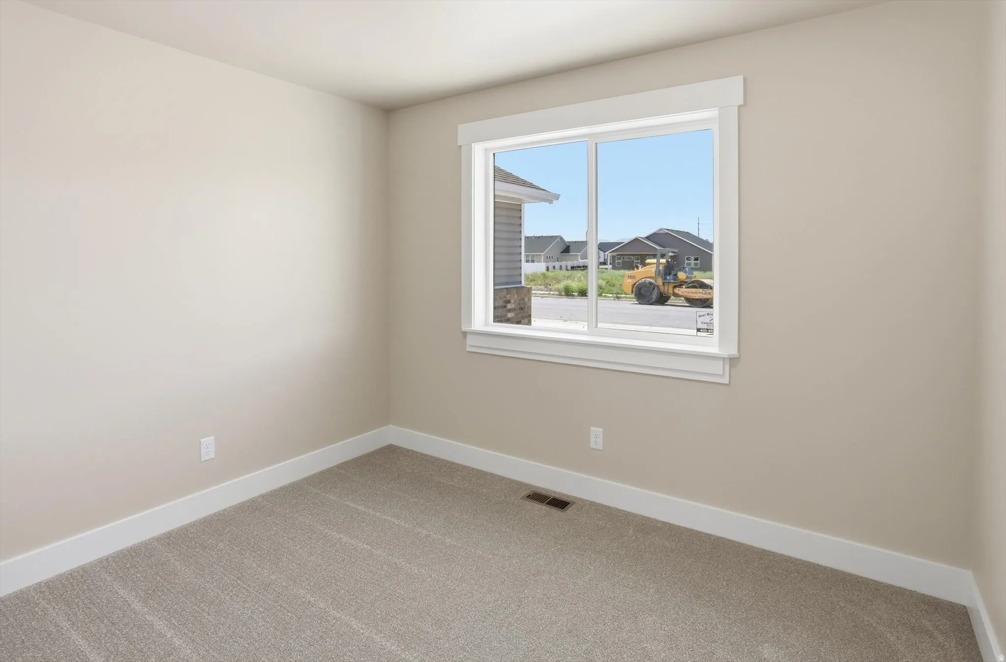 Neutral-toned interior room featuring a large horizontal window with white trim, light beige wall paint, and light gray patterned carpeting