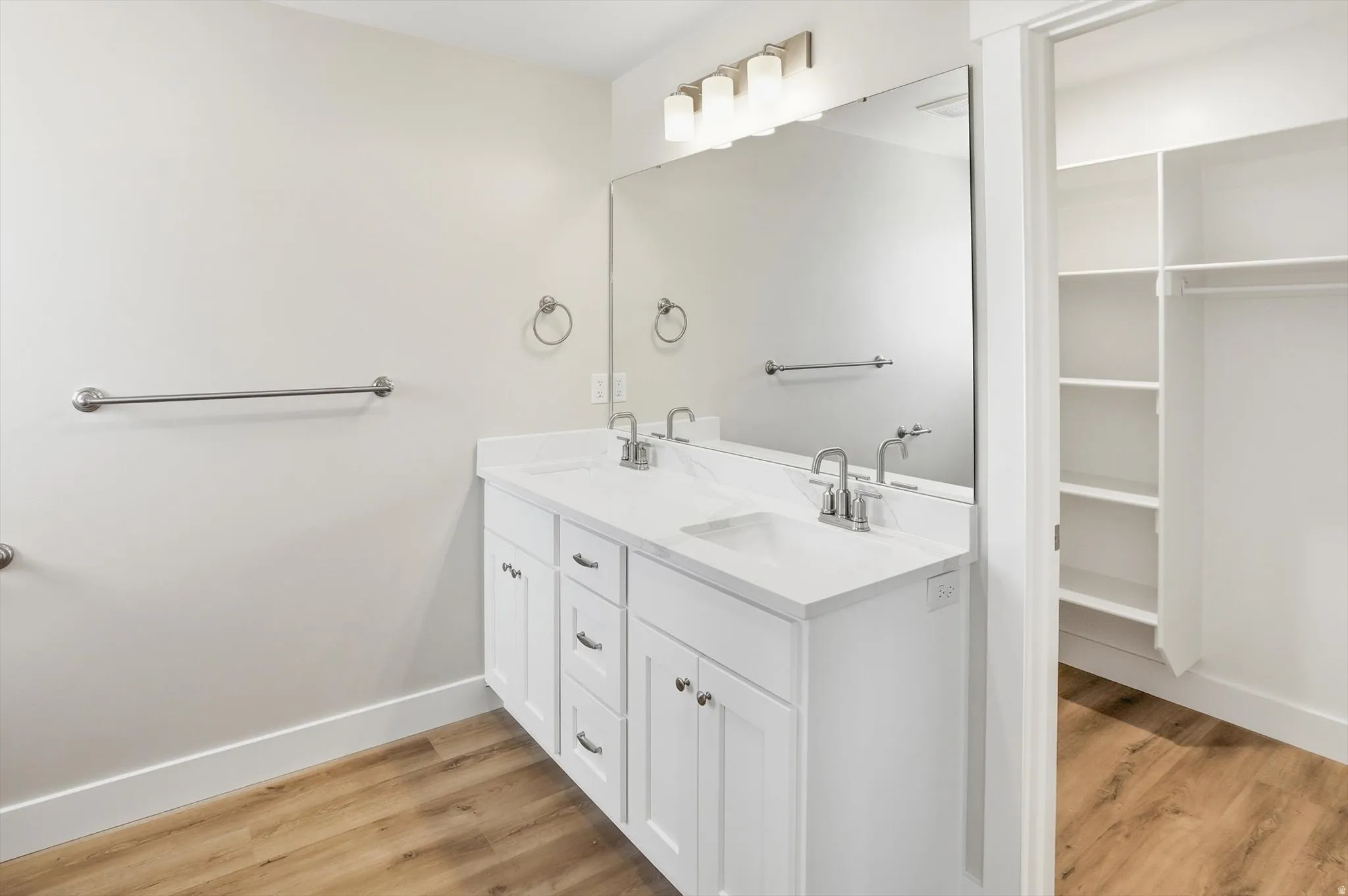 Bathroom featuring a dual vanity with white cabinetry and integrated sinks, a large mirror, and brushed nickel fixtures