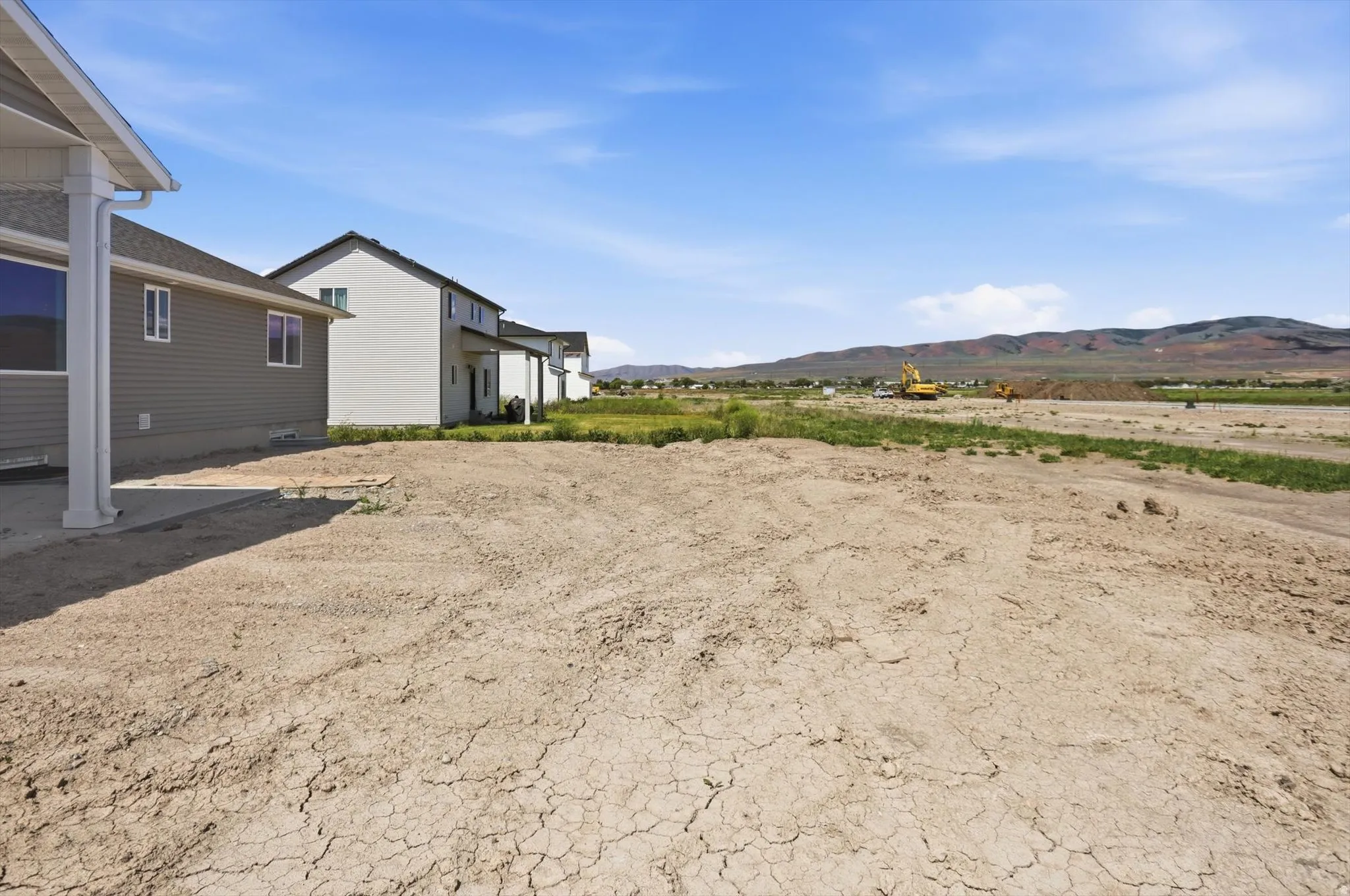 Expansive undeveloped lot with partial concrete patio and adjacent new construction residences