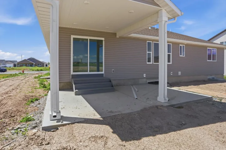 Covered concrete patio with white support columns and a gray vinyl siding exterior