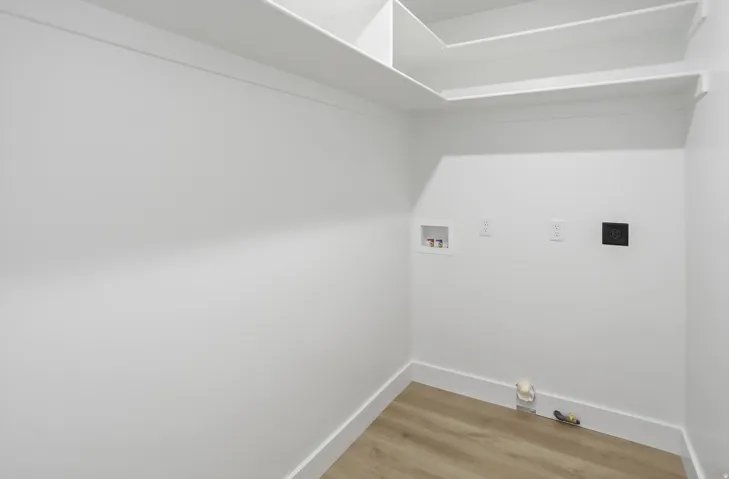 Utility room featuring wood-finish flooring, white walls, built-in shelving, and hookups