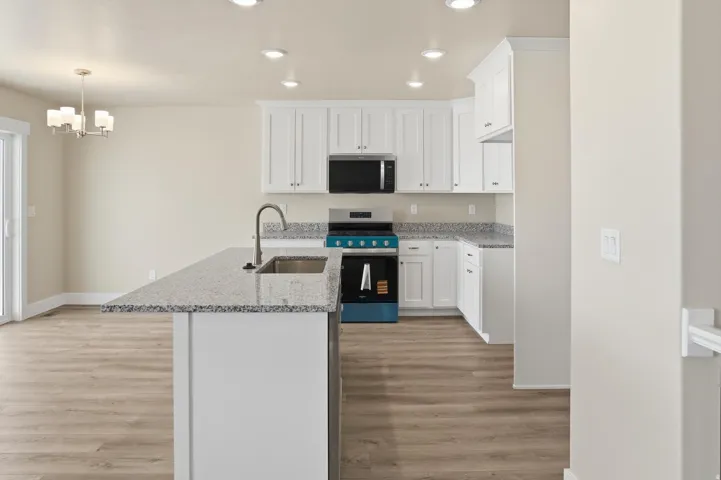 Kitchen featuring a central island with an undermount sink and faucet, white cabinetry, speckled countertops, stainless steel appliances, and wood-finish flooring