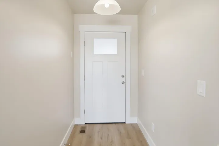 Entryway featuring a white paneled door with a rectangular window, light wood-finish flooring, light neutral-toned walls, and a ceiling-mounted light fixture