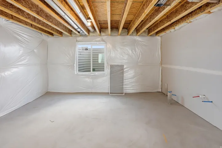 Unfinished basement space featuring exposed wood joists, concrete flooring, and a single window