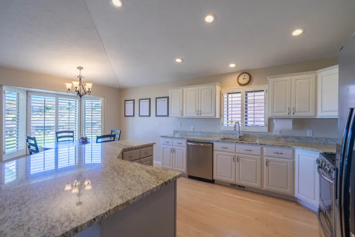 Kitchen showcasing white cabinetry, speckled countertops, stainless steel appliances, and light wood-finish flooring