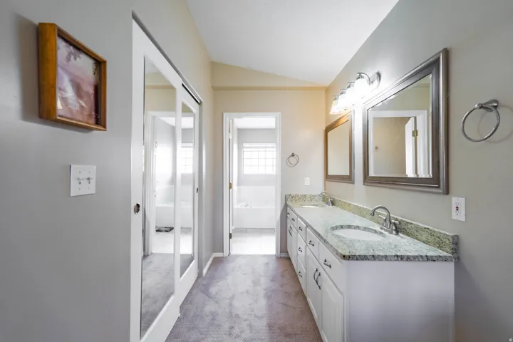Dual vanity in primary bathroom with granite countertop, individual sinks, and brushed nickel fixtures & mirrored sliding glass doors to closet