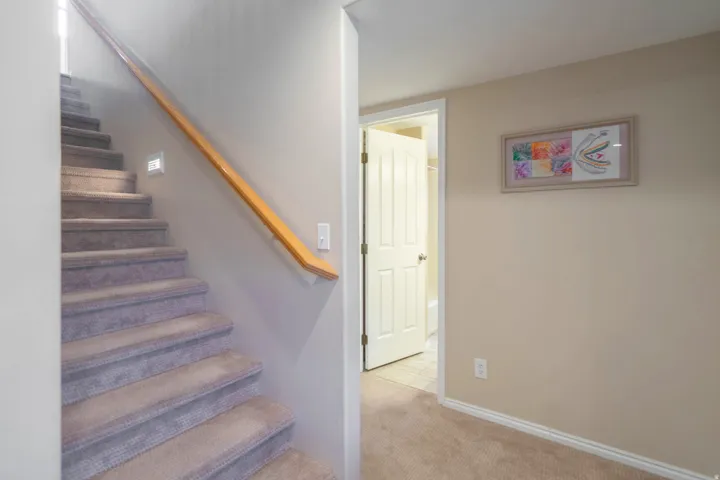 Carpeted staircase featuring a natural wood handrail and integrated step lighting with hall to bed, bath & laundry
