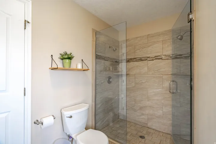 Walk-in shower in primary bathroom featuring glass enclosure, stone-look tile walls with decorative band, built-in shelving, and a coordinating tiled floor