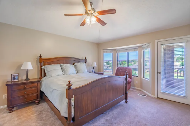 Carpeted primary bedroom featuring a ceiling fan with integrated lighting, a bay window with blinds, and a glass-paned exterior door to covered patio. Views of golf course.