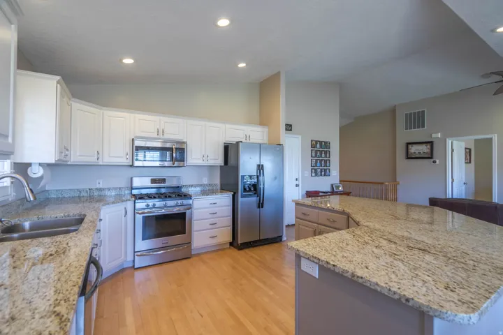 Kitchen featuring white cabinetry, stainless steel appliances, granite countertops, and wood-finish flooring