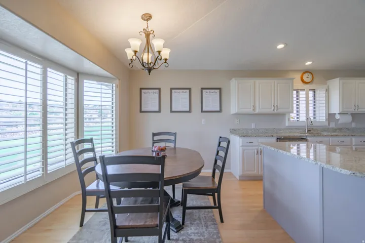 Kitchen and dining area featuring bay window with plantation shutters, light wood-finish flooring, white cabinetry, and granite countertops