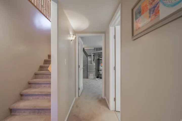 Hallway to bathroom, equipment & laundry rooms featuring neutral-toned walls, carpeted flooring, and a decorative wall sconce