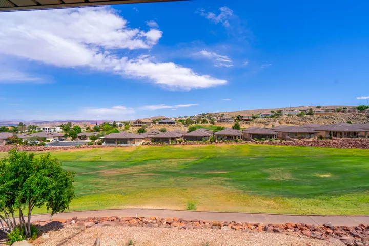 View from patio of Expansive green space bordering the property, with a paved pathway, natural rock landscaping, and distant residential structures