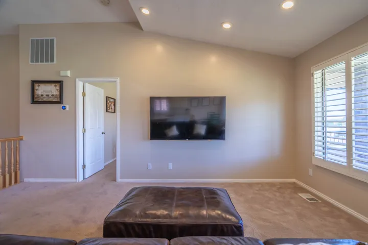Carpeted room featuring a vaulted ceiling with recessed lighting, a mounted wall screen, and a window with white plantation shutters