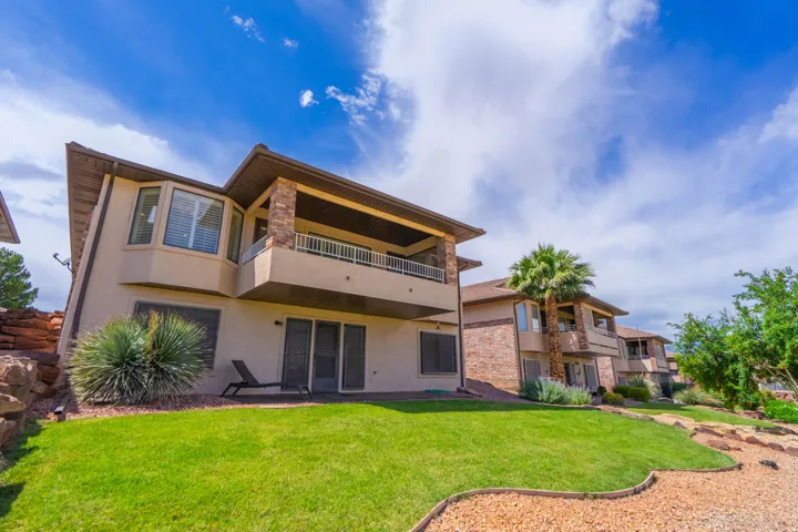 Multi-level property with a stucco exterior, a large bay window, and an upper-level balcony featuring stone pillar accents and white railings. Back yard