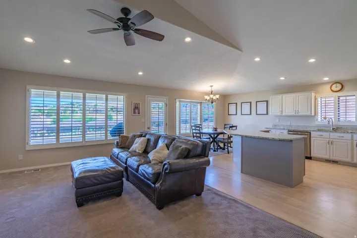Open-concept living area featuring a vaulted ceiling, plantation shutters and recessed lighting