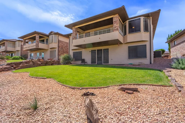 Exterior featuring a manicured lawn, gravel landscaping, a covered upper-level balcony, and a lower-level patio with sliding glass doors