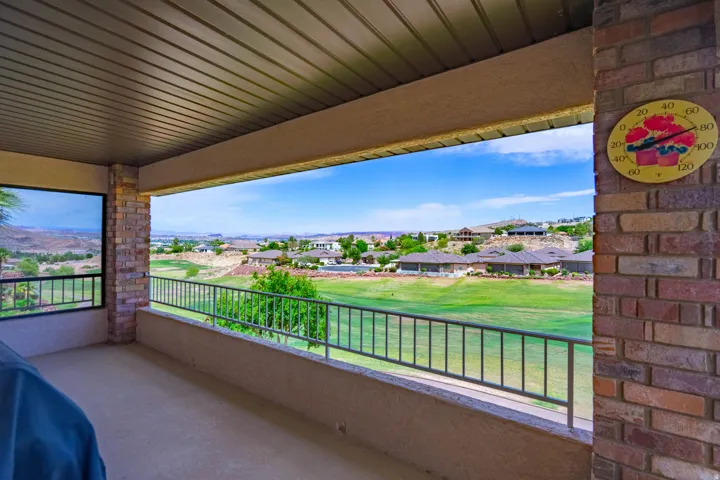 View of 13th Fairway from expansive covered patio featuring a concrete surface, metal railing, and brick pillars
