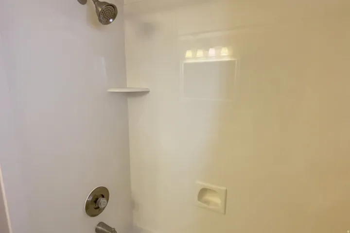 White cultured marble shower/tub combo surround with integrated shelving and soap dish. Downstairs.