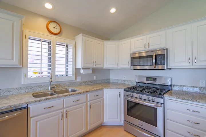 Kitchen featuring white cabinetry, light-toned granite countertops, stainless steel appliances, a double basin sink, and recessed lighting