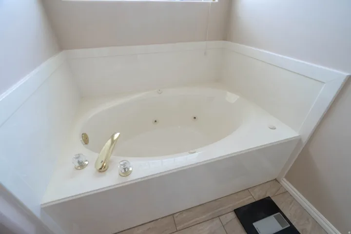 Corner jetted tub in primary bathroom featuring a gold-tone faucet, crystal-look handles, and tile flooring