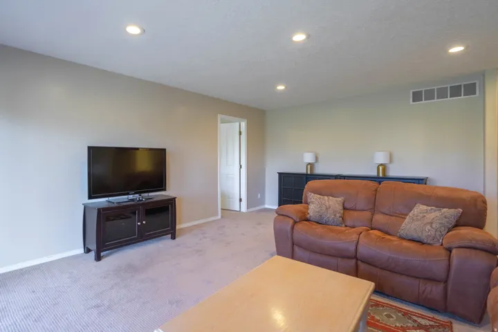 Recessed ceiling lighting illuminates the carpeted downstairs family room with neutral wall finishes. Door at back leads to 2nd Bedroom