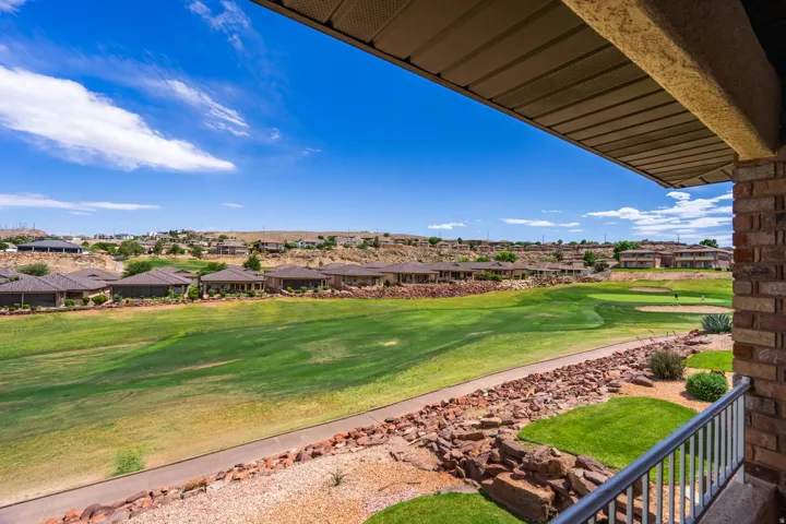 View from upper covered patio of expansive green golf course with a paved cart path bordering a rock garden