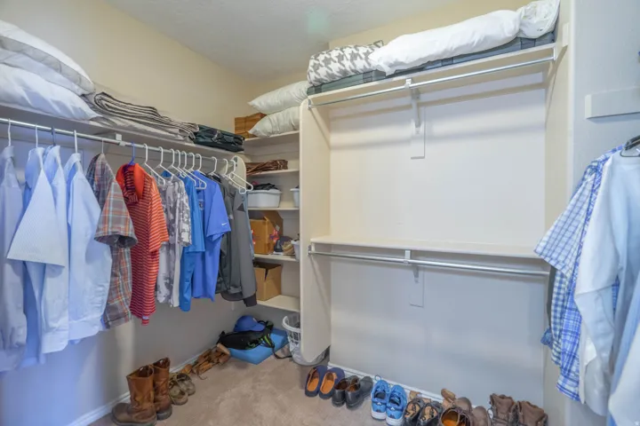 Walk-in primary closet featuring built-in shelving, multiple hanging rods, and neutral-toned carpeting