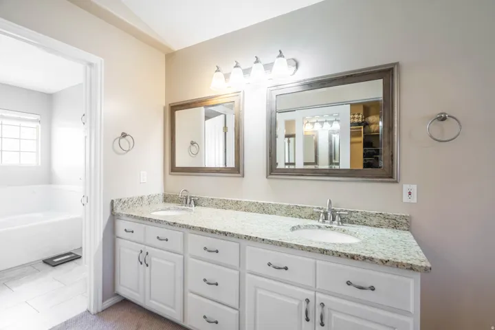 Dual vanity featuring white cabinetry with brushed nickel hardware, speckled light-toned countertop, and undermount sinks