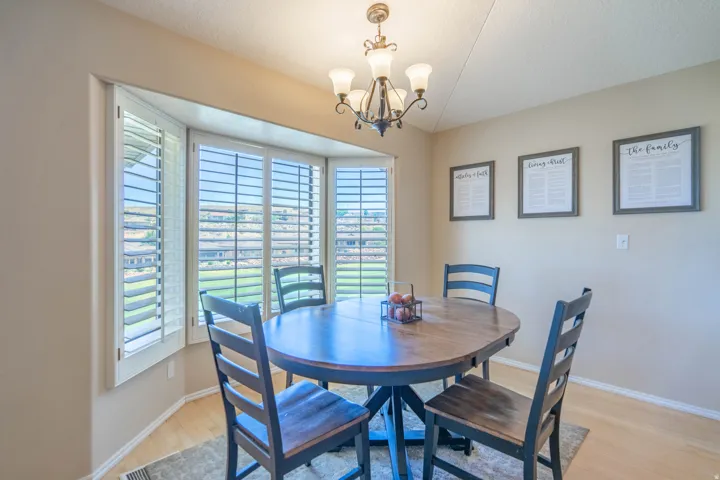 Bay window featuring plantation shutters, wood-finish flooring, a ceiling-mounted chandelier, and neutral wall tones and Views of the golf course