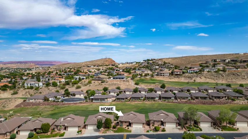 Community setting featuring a collection of homes with a desert landscape backdrop, a golf course, and distant mountains under a blue sky