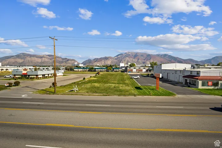 Expansive land parcel featuring clear road frontage, surrounding commercial structures, and distant mountain backdrops